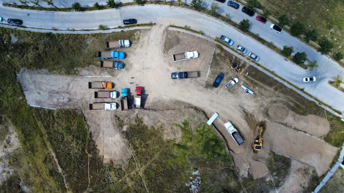 Vista aérea del frente de obra: camiones de volteo, excavadora y terreno despalmado junto al bulevar
