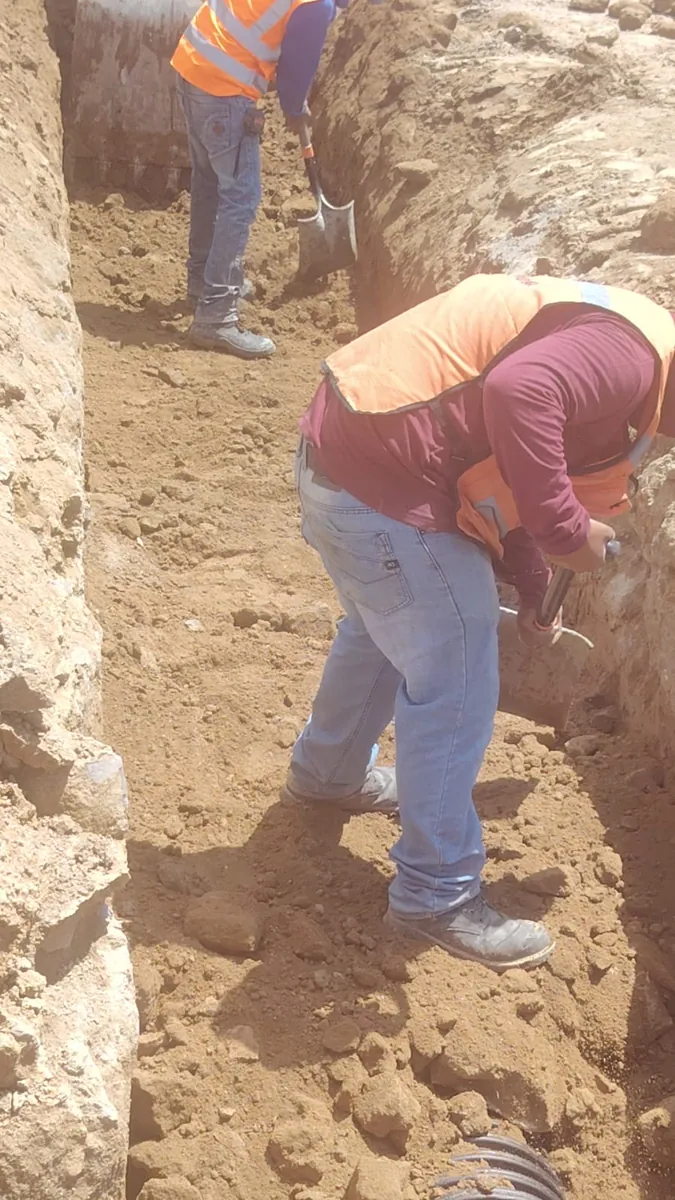 Trabajadores con chaleco naranja afinando la zanja a mano con pala